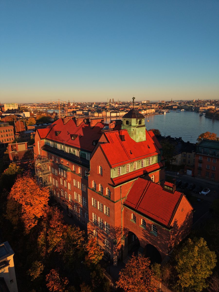 Tegelbyggnad med rött tak och kopparkupol i höstljus, med vattnet i bakgrunden